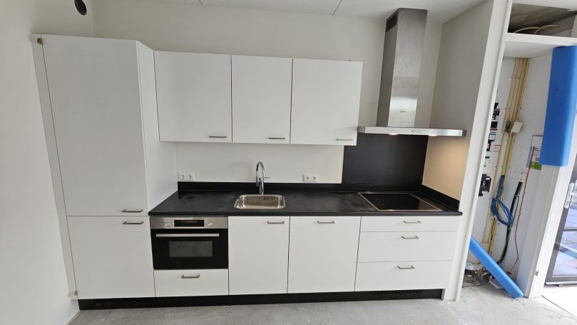Moderne, strakke witte keuken met zwarte werkbladen en ingebouwde apparatuur.
